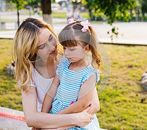 A young woman and a little girl are sitting on a bench in the park.Similarity and kinship