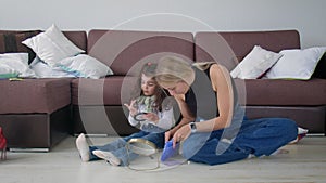 A young woman and a little girl are sitting on the floor at home and choosing cosmetics from a cosmetic bag. Beauty and