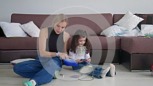 A young woman and a little girl are sitting on the floor at home and choosing cosmetics from a cosmetic bag. Beauty and