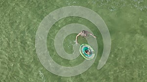 Young woman with a little girl swimming together in the ocean. View from above of the baby girl with swimming circle