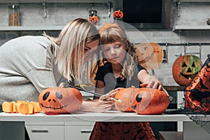 young woman and little sister painting pumpkins for halloween together in kitchen