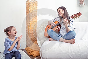 A young woman in the living room with a guitar playing for a child