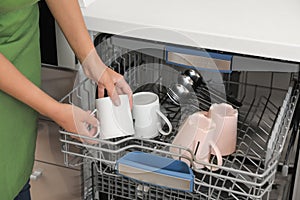 Young woman loading dishwasher in kitchen