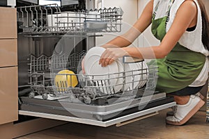 Young woman loading dishwasher in kitchen, closeup