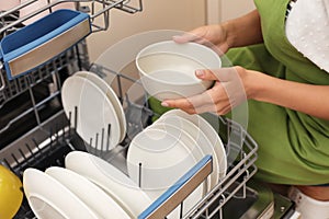 Young woman loading dishwasher in kitchen, closeup.