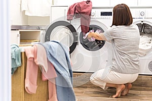 Young Woman loading washing machine and a Basket Full Of Dirty Clothes In Laundry Room