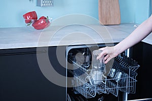 Young woman loads the dishwasher with dirty dishes