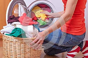 Young woman loads the laundry in the washing machine from the laundry basket before washing.