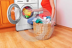 Young woman loads the laundry in the washing machine from the laundry basket before washing.