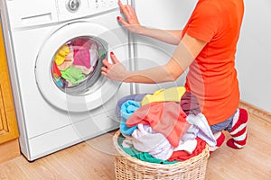 Young woman loads the laundry in the washing machine from the laundry basket before washing.