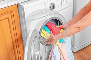 Young woman loads the laundry in the washing machine from the laundry basket before washing.