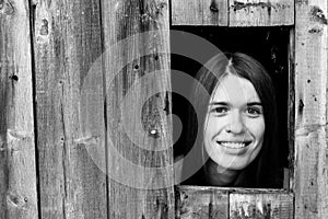 A young woman locked in a wooden shed, peeking through a small window.