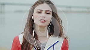 Young woman is lokking at the camera and wearing headphone for music motivation for cardio training, river on background