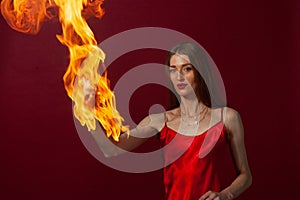 A young woman with long brown hair, in a red dress on a red background with fire