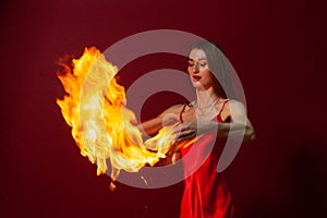 A young woman with long brown hair, in a red dress on a red background with fire