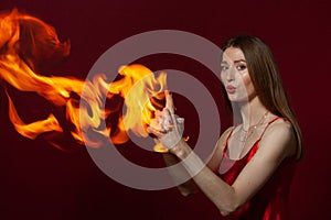 A young woman with long brown hair, in a red dress on a red background with fire