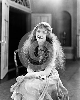 Young woman with long Curls, Curly Hair, Curly sitting on a chair and smiling