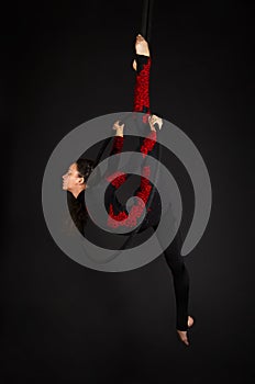 A young woman with long hair doing aerial acrobatics in a black and red suit, performs exercises in the air ring