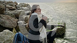 Young woman with long hair enjoying a hot tea from thermos as she takes in the stormy coastal view. Perfect for use in holiday.