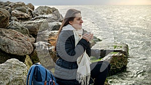 Young woman with long hair enjoying a hot tea from thermos as she takes in the stormy coastal view. Perfect for use in holiday or