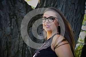 young woman long hair and eye glasses resting on tree at the park in sunshine