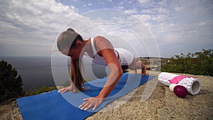 Young woman with long hair, fitness instructor in white sportswear, doing stretching and pilates on yoga mat in the park