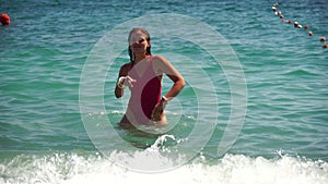 Young woman with long hair in a red swimsuit and bracelets in boho style enjoying the waves on the beach in summer