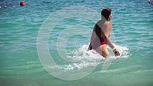 Young woman with long hair in a red swimsuit and bracelets in boho style enjoying the waves on the beach in summer