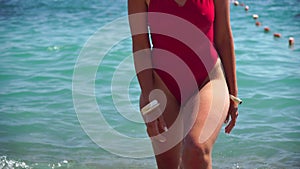 Young woman with long hair in a red swimsuit and bracelets in boho style enjoying the waves on the beach in summer
