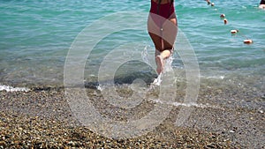 Young woman with long hair in a red swimsuit and bracelets in boho style enjoying the waves on the beach in summer