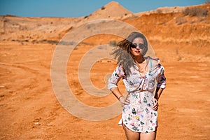 A young woman with long hair in a short dress walks through the orange rocky desert on a hot day