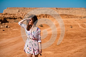 A young woman with long hair in a short dress walks through the orange rocky desert on a hot day