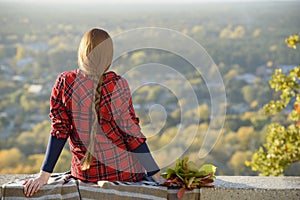 Young woman with long hair sits on a hill overlooking the city photo