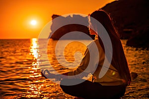 Young woman with long hair in sportswear and boho style braclets practicing outdoors on yoga mat by the sea on a sunset