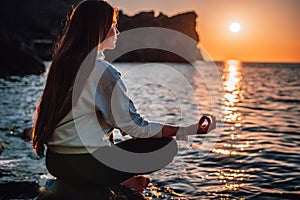 Young woman with long hair in sportswear and boho style braclets practicing outdoors on yoga mat by the sea on a sunset