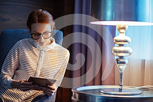 Young woman with long hair using tablet and smiling sitting on sofa