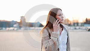 Young woman with long hair walks along the street and talks on the phone