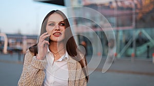 Young woman with long hair walks along the street and talks on the phone