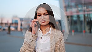 Young woman with long hair walks along the street and talks on the phone