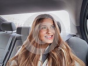 Young woman with long hair, wavy hairstyle in the car or taxi cab as passenger, exploring the city, transport and travel