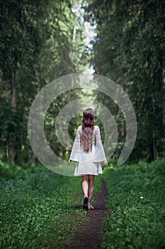 A young woman with long hair in a white dress walks along a path into the forest, an abyss concept, getting lost, danger