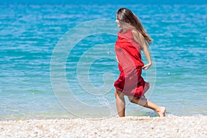 Young woman in long red dress running along seashore