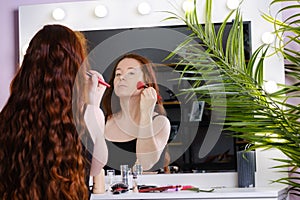 Young woman with long red hair preens in front of a mirror
