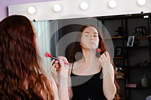 Young woman with long red hair preens in front of a mirror