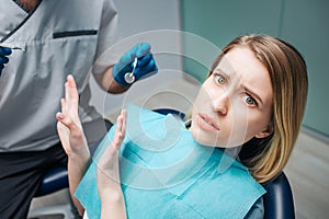Young woman look afraid. She sit in chair in dentistry. Woman look on camera and push away doctor. He hold dentist`s