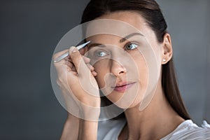 Young woman look in mirror pinch eyebrows with tweezers