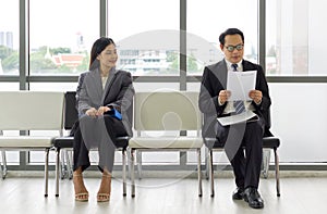 Young woman look and smile at a man sitting further away. Asian business people waiting for job interview by sitting spaced apart