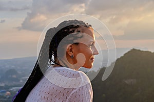Young woman looking at amazing sunset in mountains. Cornrows hairstyle