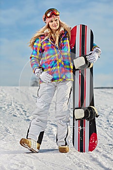 Young woman looking away while holding snowboard in snow