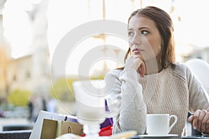 Young woman looking away while sitting at sidewalk cafe